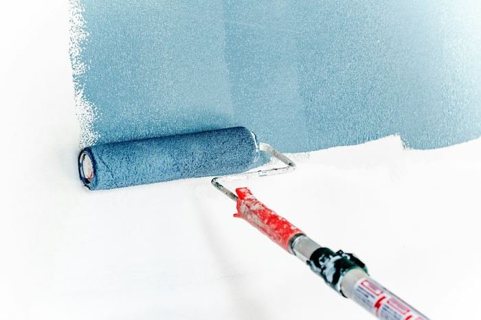 Farbroller trägt blaue Farbe auf eine weiße Wand auf