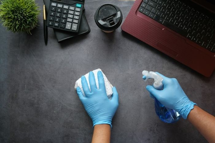 Hände in Schutzhandschuhen reinigen eine Schreibtischfläche